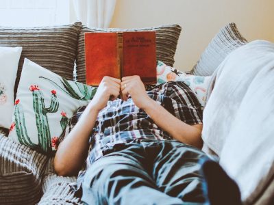 photo of man lying on bed while reading book