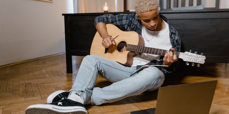 teenage boy sitting on the floor while playing guitar